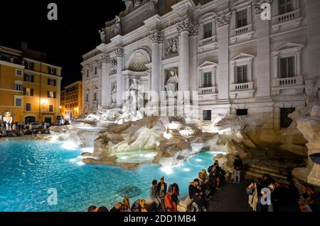 Vista serale mentre i turisti si godono la Fontana di Trevi illuminata di colori Nel centro di Roma Foto Stock