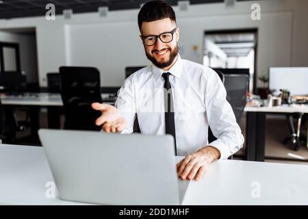 Giovane uomo d'affari che parla in conferenza web con i colleghi utilizzando la webcam del laptop, un dipendente maschio che parla in videochiamata con i colleghi Foto Stock