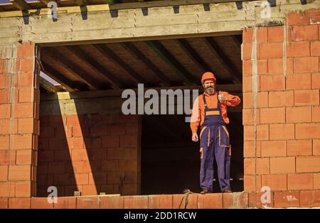 Abbastanza per oggi. Routine quotidiana alla costruzione. Bravo. Riparatore stanco costruttore rilassante in cantiere. Pausa e relax. Uomo barbuto in uniforme ingegnere e elmetto. Giorno normale. Foto Stock