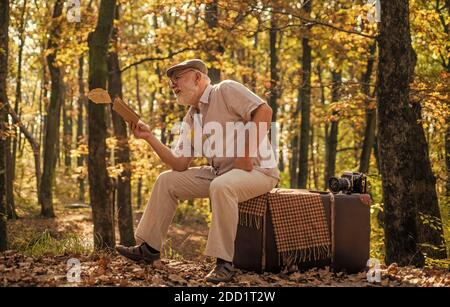 Avere il piacere di leggere di più. Pensionato leggere libro in autunno natura. Il vecchio leggeva seduto su una valigia retrò. Letteratura e biblioteca. Conoscenza e informazione. Gita naturalistica. Basta leggere bene. Foto Stock