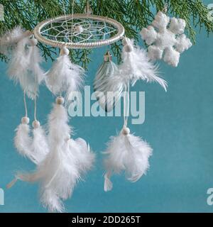 Dreamcachter bianco con piume e natale bauble appeso sul ramo di thuja. Amuleto nativo americano, simbolo e patrimonio. Foto Stock