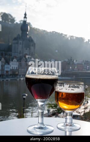 Bere birra abbaziale belga scura e forte con formaggi in giornata di sole con bella vista sul fiume Maas e città Dinant, Belgio Foto Stock