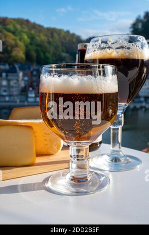 Bere birra abbaziale belga scura e forte con formaggi in giornata di sole con bella vista sul fiume Maas e città Dinant, Belgio Foto Stock