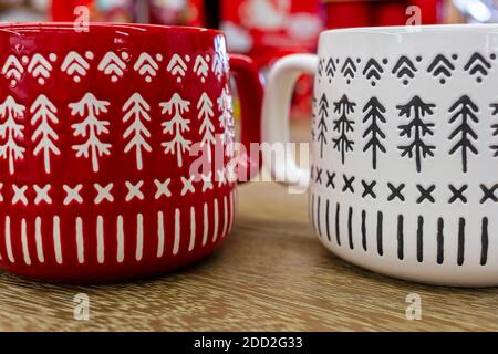 Immagine in primo piano di due tazze di caffè in porcellana (rossa e bianca) poste su un tavolo di legno. Entrambe le tazze hanno le figure dell'albero di natale del pino come pa ripetuto Foto Stock