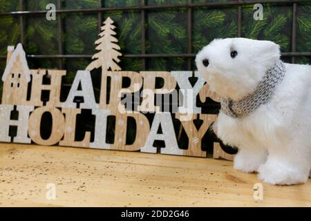 Una decorazione di natale con un messaggio di buone feste scritto usando le lettere di legno e un giocattolo peluche dell'orso polare carino vicino ad esso. Sono messi su un legno Foto Stock