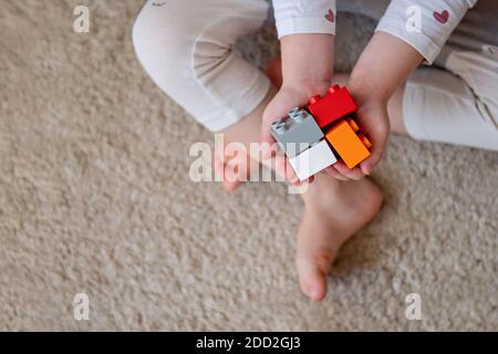 Un bambino piccolo tiene nelle palme dei blocchi di costruzione dell'arcobaleno. Mani di capretto con giocattolo di mattoni su sfondo beige. Giocattoli educativi colorati. Piatto Foto Stock