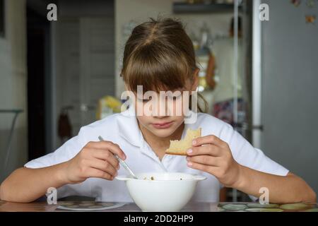 Una studentessa venne da scuola e si sedette a mangiare al tavolo in cucina a casa Foto Stock