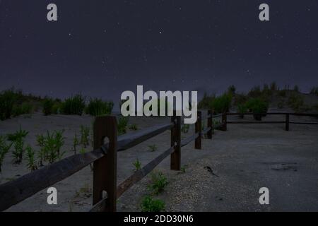 Un percorso in spiaggia con una recinzione sul lato e. Un cielo notturno pieno di stelle Foto Stock