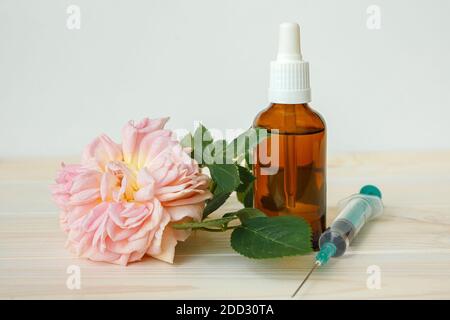 Rosa e flacone con olio aromatico o medicinale e siringa su un tavolo di legno bianco Foto Stock
