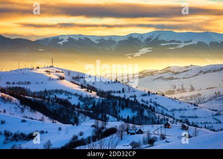 paesaggio invernale in montagna all'alba. bella zona rurale dei monti carpazi con colline innevate. nuvole incandescenti sul cielo. verdore gelide Foto Stock