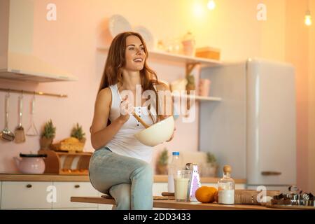 Bella donna in camicia bianca che mescola qualcosa in una ciotola e aspetto positivo Foto Stock