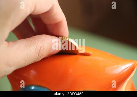 La mano mette la moneta in una scatola salvavita arancione. Risparmio di denaro e concetto finanziario di investimento. Foto Stock