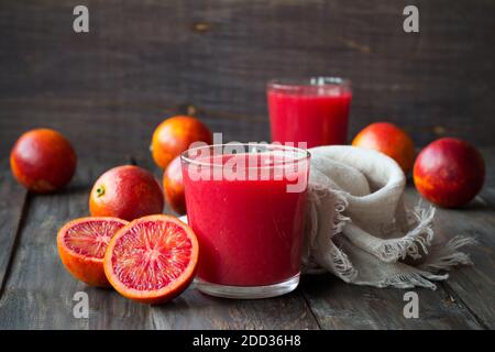 Spremuta fresca di arance di sangue in vetro con arance fresche intere su un tavolo di legno, fuoco selettivo Foto Stock