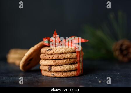 I biscotti shortbread con pezzi di cioccolato sono legati con un bel nastro rosso su uno sfondo scuro. Un luogo per il testo. Cookie di Capodanno. Foto Stock