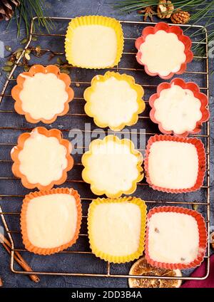 Preparazione di impasto crudo per muffin alla vaniglia in stampi di diverse forme. Noci, bastoncini di cannella, uvetta, ciuffi mangiati. Le delizie di Capodanno. Disposizione piatta Foto Stock