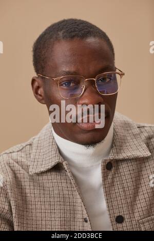 Ritratto di giovane africano in occhiali ed in elegante vestiti che guardano la macchina fotografica isolata su sfondo beige Foto Stock