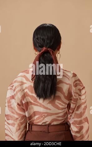 Vista posteriore della giovane donna con capelli lunghi e scuri legati con nastro sullo sfondo beige Foto Stock