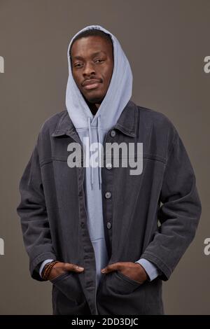 Ritratto di uomo africano in felpa con cappuccio e giacca jeans posa in posa sulla telecamera isolata su sfondo grigio Foto Stock