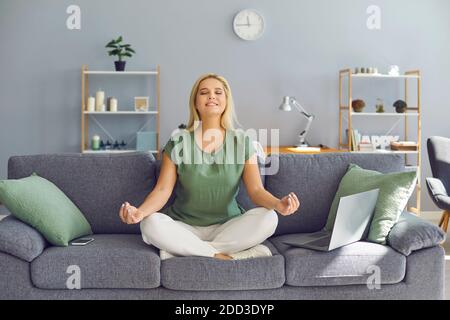 Donna d'affari sorridente e rilassata che medita mentre lavora a casa seduto vicino al computer portatile sul divano. Foto Stock