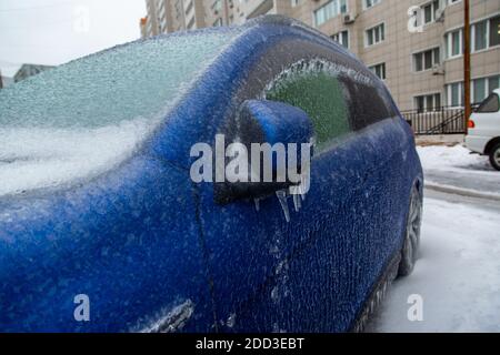 L'auto blu è coperta da una spessa crosta di ghiaccio, gelida pioggia, in città. Foto Stock