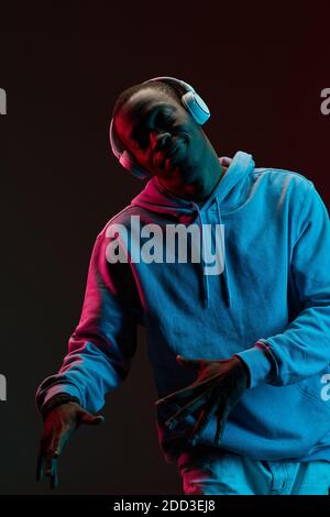 Uomo africano in cuffie wireless che balla contro lo sfondo nero Foto Stock