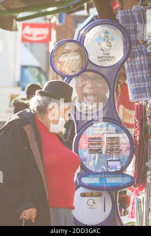 Londra, Regno Unito - 3 novembre 2020 - Stand National Lottery e una donna anziana con maschera a Walthamstow Foto Stock