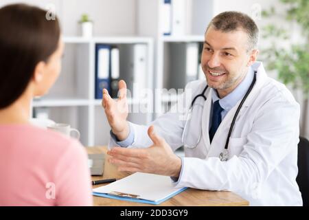 Medio invecchiato sorridente medico esperto che parla con il suo paziente Foto Stock