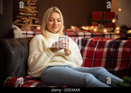 Donna felice a casa che legge un messaggio di testo mentre si siede sul divano in festa di Natale, felice anno nuovo Foto Stock