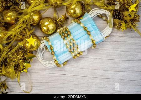 Composizione con maschera medica blu corona virus e decorazione invernale con palline d'oro su sfondo di legno offuscato. Buon Natale in covid-19 pa Foto Stock