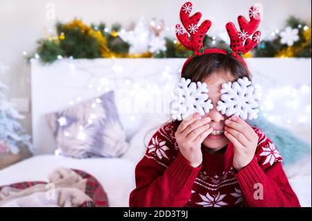 Una bambina in un maglione di Natale gioca con i fiocchi di neve di Capodanno. Buon bambino in una stanza di luce di festa. C'è un posto per la copia dell'annuncio. Concetto di vacanza invernale. Foto di alta qualità Foto Stock