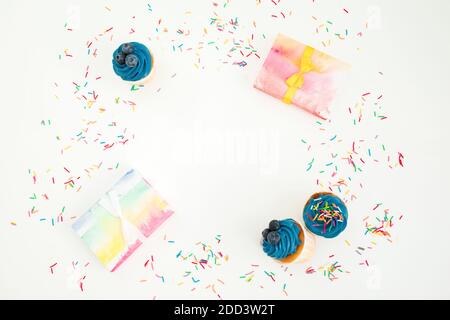 Muffin ai mirtilli con scatola regalo di crema e arcobaleno su sfondo bianco. Disposizione piatta, vista dall'alto. Spazio di copia Foto Stock