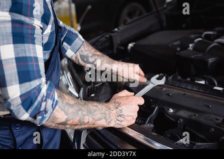 vista parziale della chiave di ritegno del tecnico tatuata vicino al motore dell'auto compartimento in primo piano sfocato Foto Stock