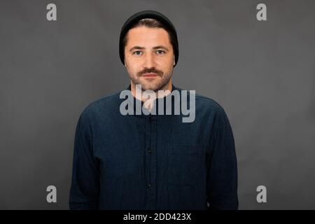 Bell'uomo senza barba con cappuccio in maglia che si pone sul grigio studio sfondo Foto Stock