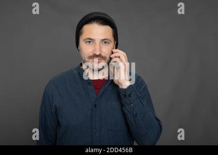 Bell'uomo senza barba con cappuccio in maglia che parla al telefono su studio grigio Foto Stock
