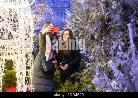 Mosca / Russia - Dicembre 2019: Festa di Capodanno a Mosca sulla piazza rossa di notte. Due giovani amiche prendono un selfie vicino a tre di Natale Foto Stock