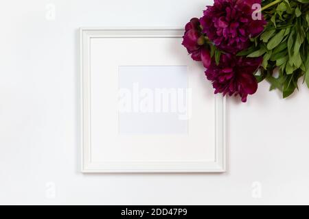 Cornice quadrata bianca con bouquet di peonie su sfondo bianco, spazio copia. Vista laterale o piatta, mockup minimal style. Per negozio di articoli da regalo, social media, Foto Stock