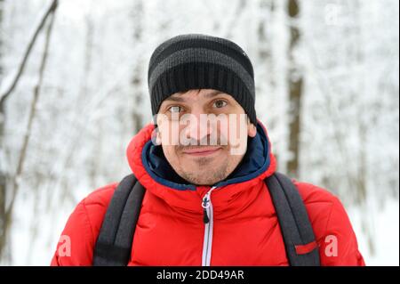 ritratto di un giovane felice in giacca rossa e cappello in una foresta invernale innevata Foto Stock