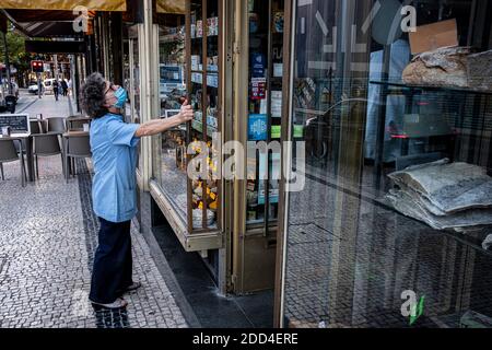 Porto, Portogallo - 27 Agosto 2020 : dipendente che controlla la finestra del suo negozio di alimentari Foto Stock