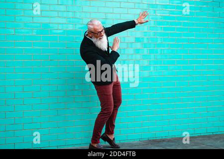 Felice maschio che festeggia. Energico felice uomo maturo in abiti casual, parete isolata in fondo azzurro. Concetto di stile di vita gioioso per anziani. Messa a fuoco Foto Stock