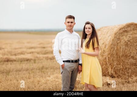 Foto di gioiosa coppia uomo e donna che camminano attraverso il campo d'oro con un mazzo di fiati e si abbracciano insieme durante il giorno di sole. Foto Stock