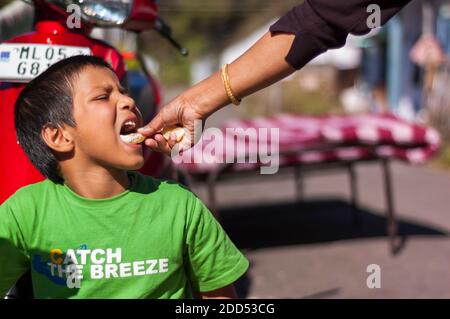 Un ragazzo di etnia indiana asiatica viene nutrito da sua nonna una fetta di arancio, che non è nella foto. Foto Stock