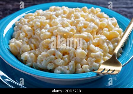 primo piano di mac e formaggio in una ciotola blu con forchetta dorata e tovagliolo su un tavolo di legno, vista orizzontale dall'alto Foto Stock