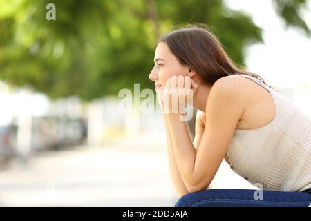 Profilo di una donna penosa che contempla seduta in una panchina Foto Stock