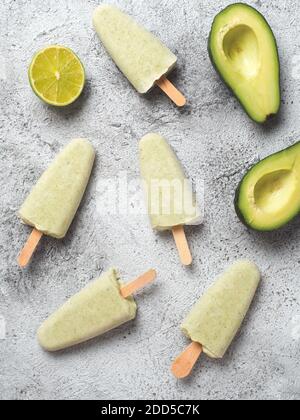 Pop sicle di avocado di tiglio vegano crudi fatte in casa. Gelato verde senza zucchero, non caseario su sfondo grigio. Vista dall'alto. Idee e ricette per spuntini sani, dessert o frullati. Verticale. Foto Stock