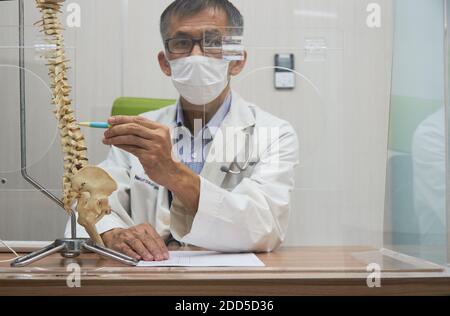 Un neurochirurgo che usa la penna che punta al modello della colonna vertebrale umana in studio medico durante la pandemia di covid-19 Foto Stock