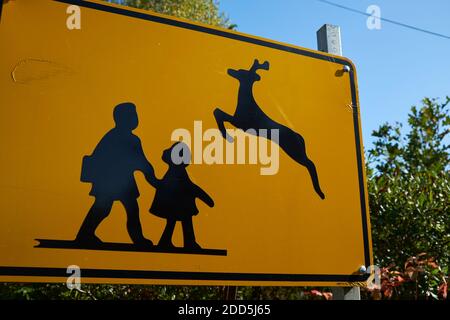 Un cartello giallo di avvertimento per la strada con una divertente giustapposizione dei bambini della scuola e dei cervi che saltano attraverso immagini grafiche. Su Deer Isle, Maine. Foto Stock