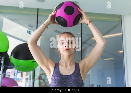 Ragazza giovane bionda sportiva fa un esercizio con palla med in palestra Foto Stock