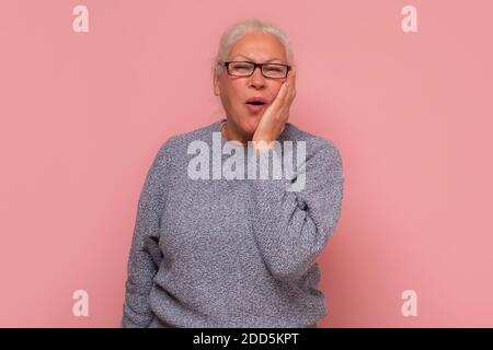 Donna anziana con mal di denti che tiene la guancia. Studio girato su parete rosa. Foto Stock