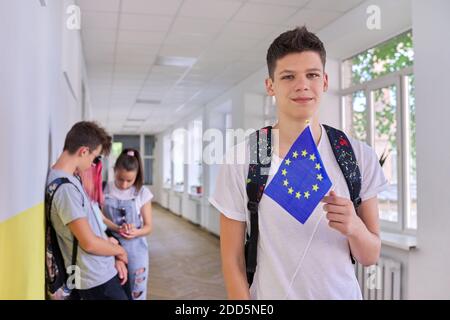 Studente maschile adolescente con bandiera UE all'interno del college, gruppo di studenti background Foto Stock