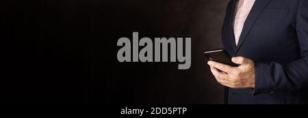Contattaci concetto di connessione con spazio di copia. Mano di un uomo d'affari che tiene un cellulare. Sfondo scuro Foto Stock